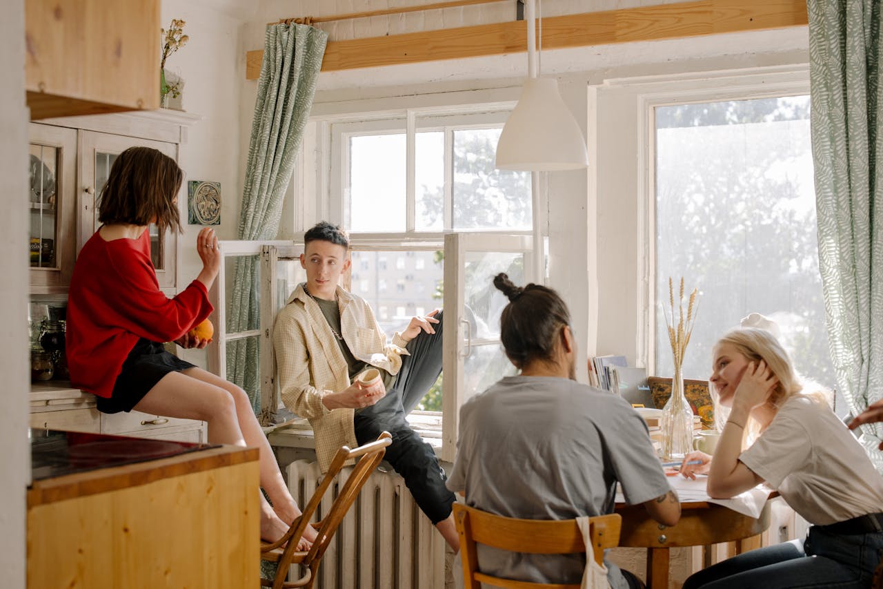 Group of young friends relaxing and chatting in a sunlit kitchen space.