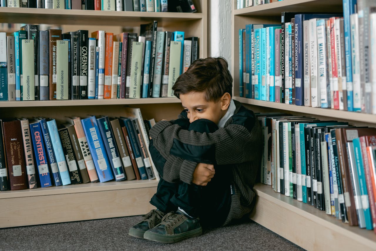 Young boy in library appears sad, sitting alone among bookshelves, suggesting themes of solitude and bullying.