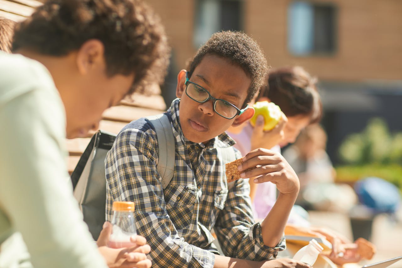 Children having lunch outdoors, engaging in conversation and eating snacks.